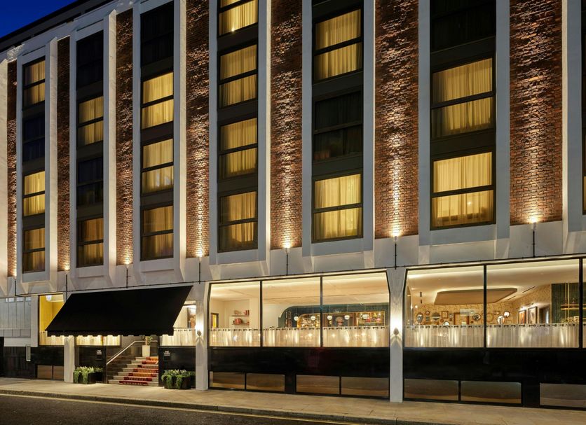 The Cura Hotel Kensington, London exterior with illuminated windows and glass-fronted ground floor