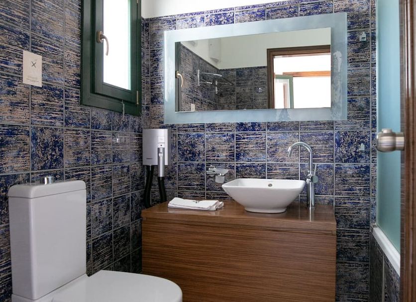 Krinos Suites Andros bathroom with vessel sink, wood vanity, mirror, and tiled walls in Andros