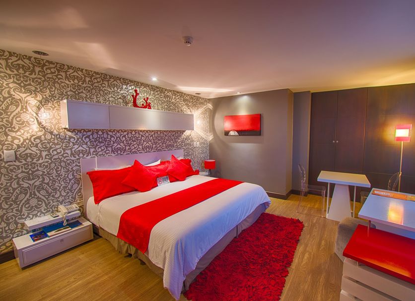 Rioné Hotel Boutique in Cuenca guest room with red accents, bed, desk and patterned wall