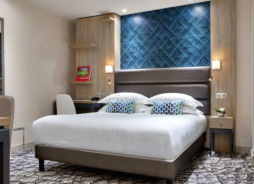Serotel Suites Paris guest room with double bed, blue headboard accent wall and patterned carpet