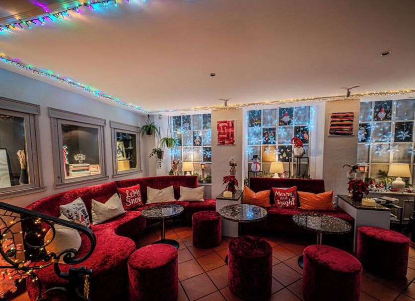 Roesli Guest House Lucerne lounge with red velvet seating, round tables and festive string lights