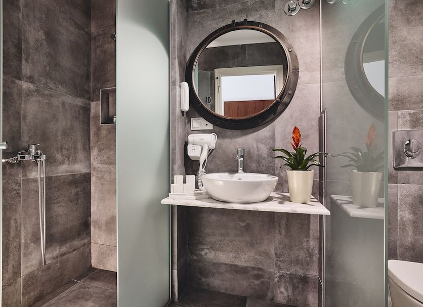 Capetan Giorgantas in Adamantas bathroom with round mirror, vessel sink and glass shower