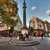 Victory House London in London near a busy plaza with a tall monument and surrounding historic buildings