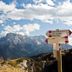 Hotel Pinzolo-Dolomiti in Pinzolo with mountain peaks and a trail sign under a partly cloudy sky