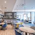 Hampton by Hilton Oswiecim breakfast seating area with round tables, blue and yellow chairs, and pendant lights