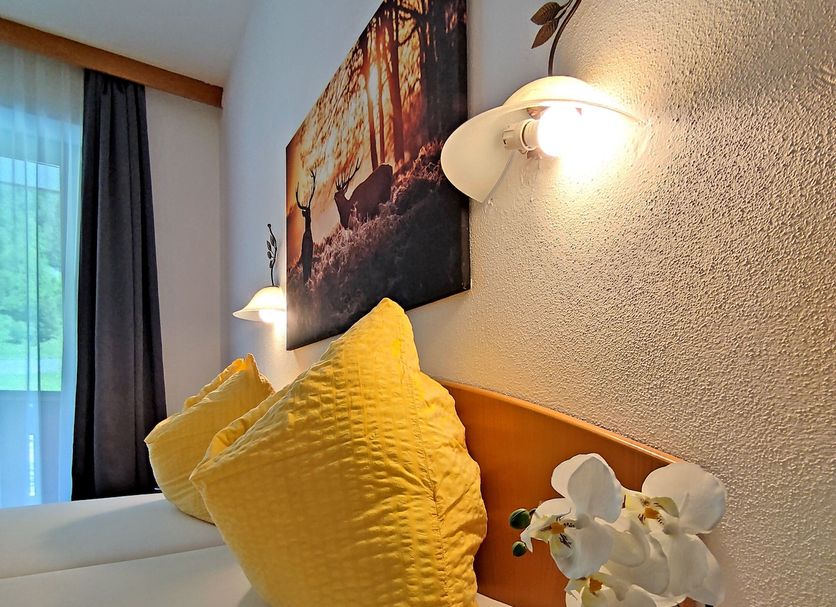 Hotel Wasserfall in Fusch an der Grossglocknerstrasse: cozy guest room with yellow pillows and wall lamp