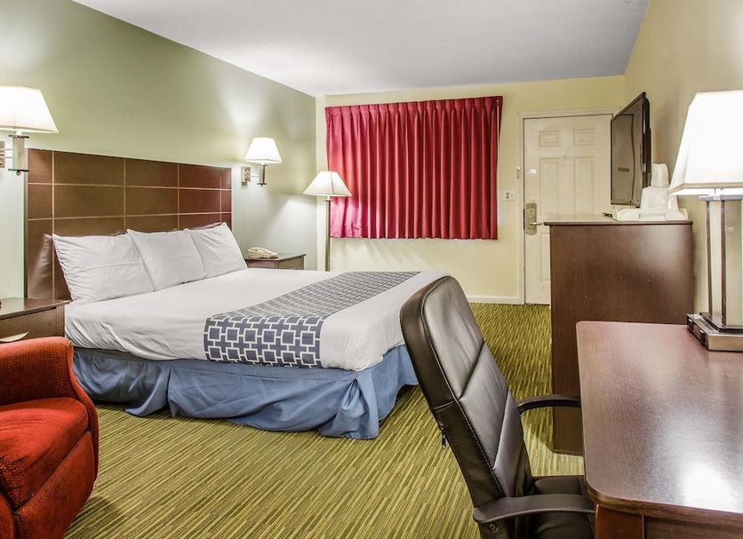 Rodeway Inn Groton guest room with king bed, desk, red chair, and red curtains