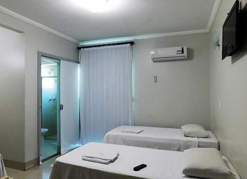 Hotel Minas in Três Marias guest room with two single beds, TV, air conditioner, and bathroom door