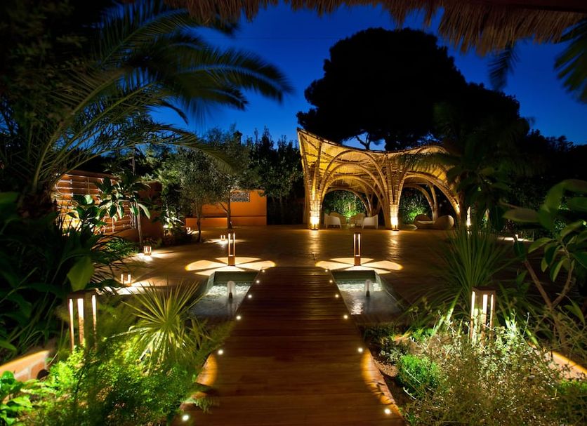 Hotel Mr Les Rotes in Denia: illuminated garden walkway with wooden deck and arched outdoor lounge at night