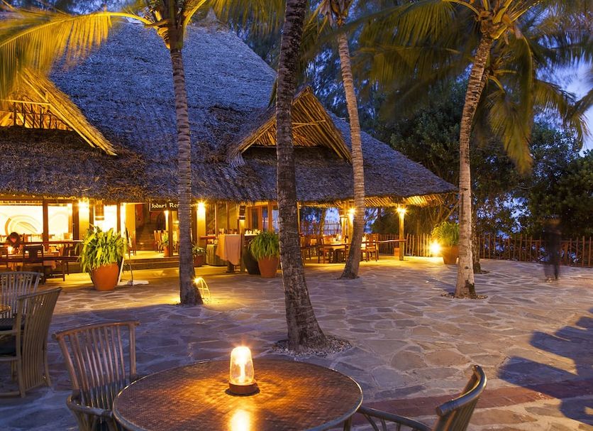 Baobab Beach Resort & Spa in Ukunda, palm-lined patio with thatched dining area at dusk