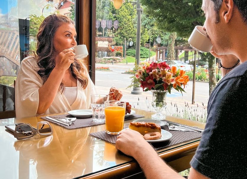 Hotel Vovó Carolina, Gramado: two guests drinking coffee at a window table with breakfast and flowers