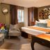 Hôtel Baume in Paris guest room with two armchairs, bed, and balcony doors opening to greenery