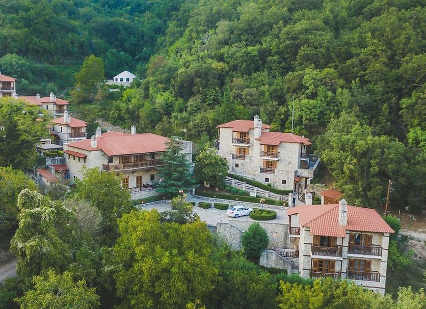 Abeliona Retreat in Ambeliona hillside hotel amid lush green trees and red-roofed buildings