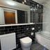 Tre-Ysgawen Hall & Spa bathroom in Llangefni with black tile, bathtub, toilet, and glass shower screen