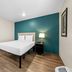 Woodspring Suites San Antonio South guest room with bed, teal accent wall, and wood-look flooring