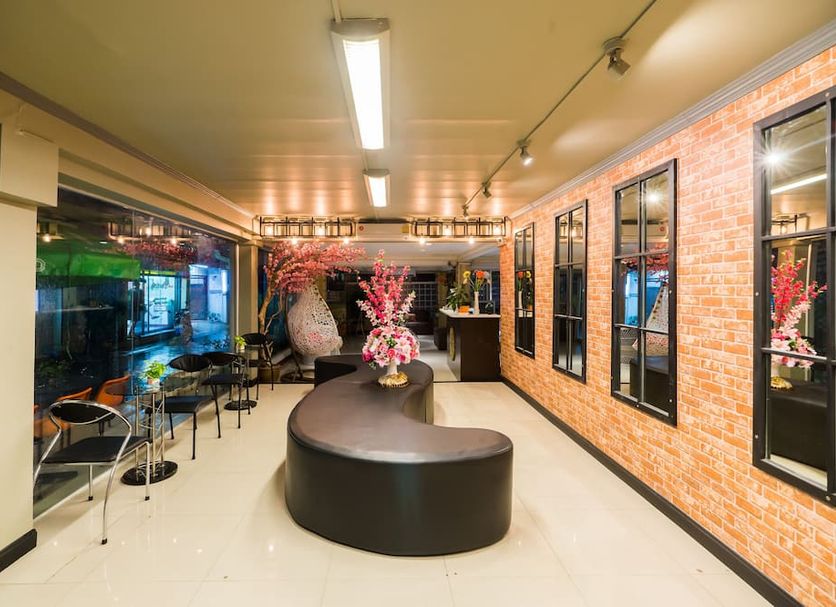 The Corner Ratchada in Bangkok lobby with curved black seating, glass wall, brick accent wall, and café tables
