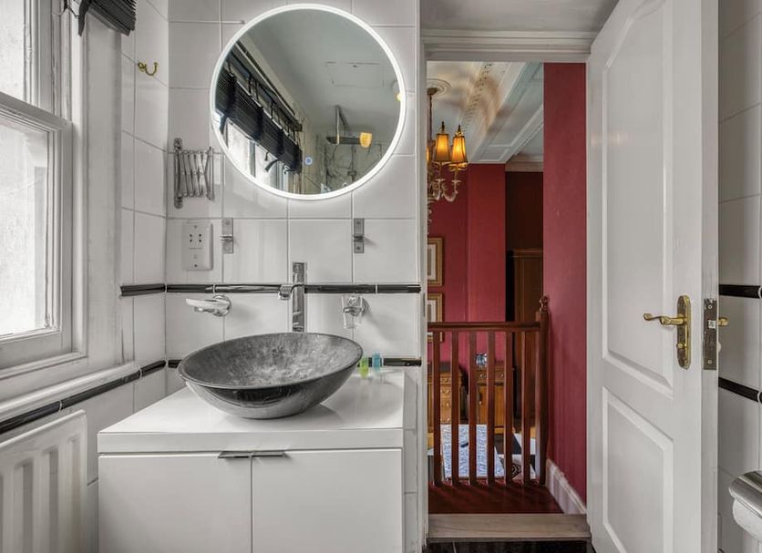 Opulence Boutique Hotel London bathroom with round mirror, vessel sink and view into a red hallway