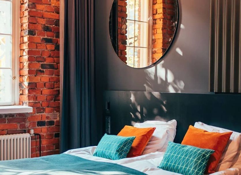 The Folks Hotel Konepaja in Helsinki guest room with exposed brick wall, round mirror, and colorful bed pillows
