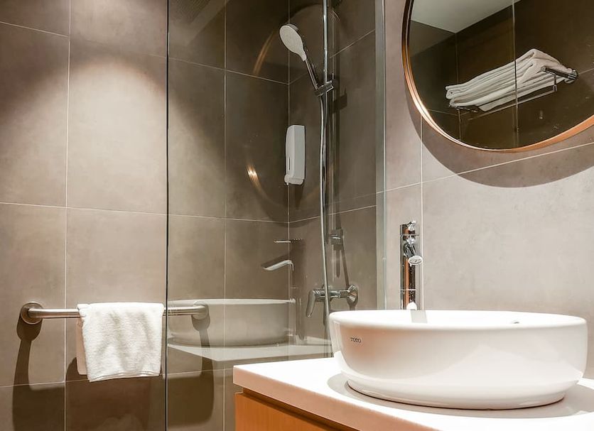 Caritas Oswald Cheung International House bathroom with glass shower, vessel sink, towel rack and round mirror in Hong Kong