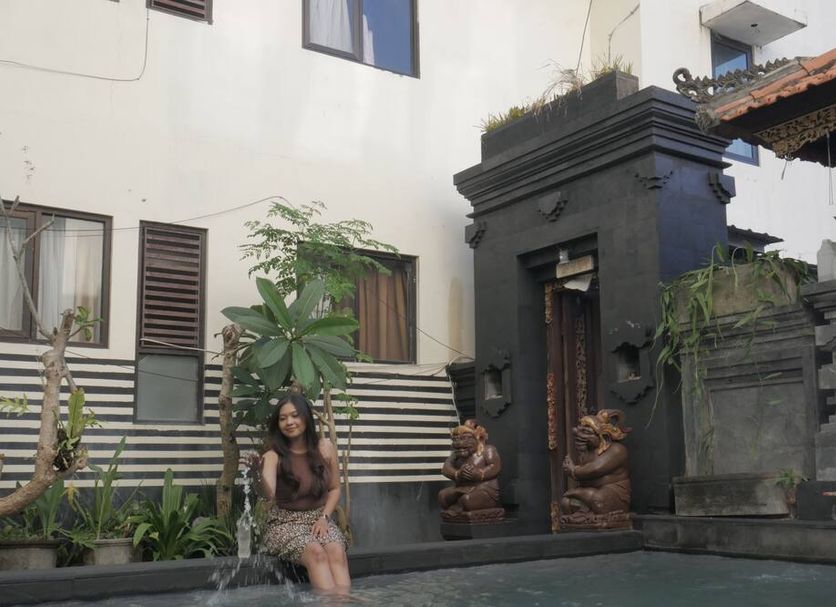 Suardana Inn's in Kuta courtyard with potted plants, stone gate, and guest walking outside