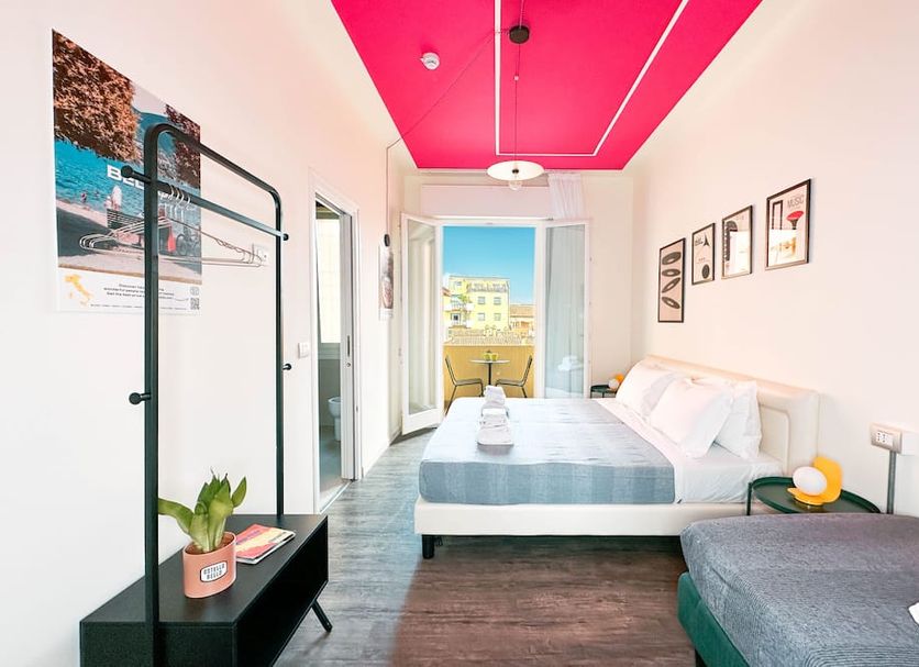 Ostello Bello Bologna room with bright pink ceiling, bed, balcony view, and small sitting area in Bologna
