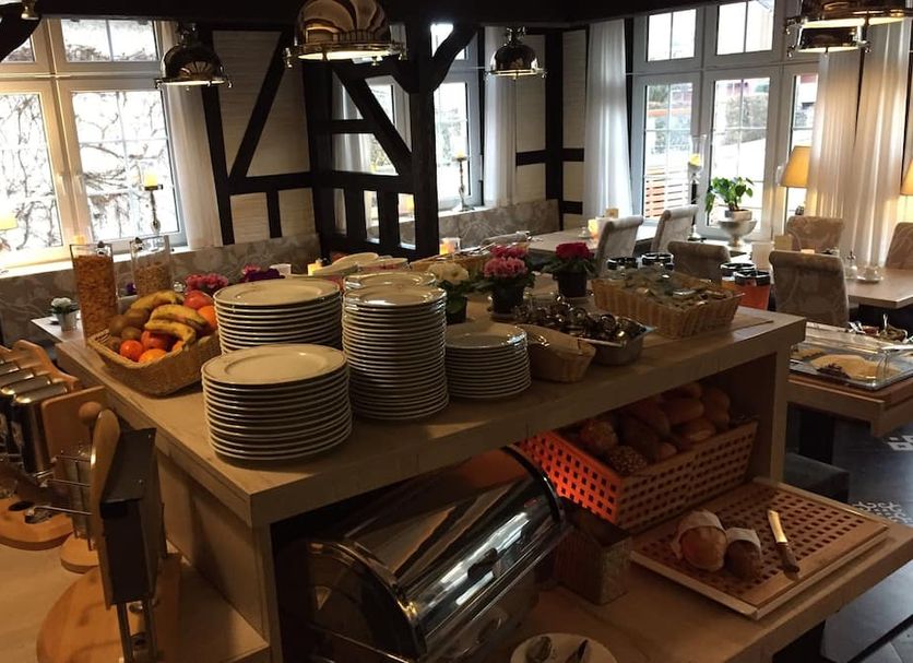 Hotel Haase in Laatzen breakfast buffet with stacked plates, pastries, fruit, and dining room windows