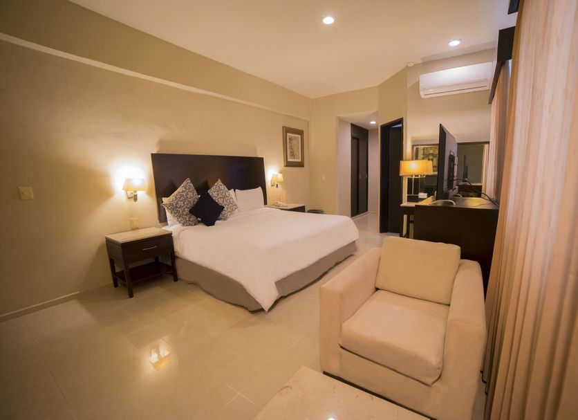 Hotel Grand Marlon in Chetumal guest room with king bed, armchair, and vanity mirror