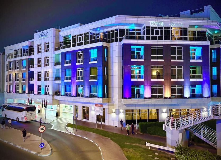 TIME Grand Plaza Hotel in Dubai at night with blue and purple-lit exterior and curved driveway