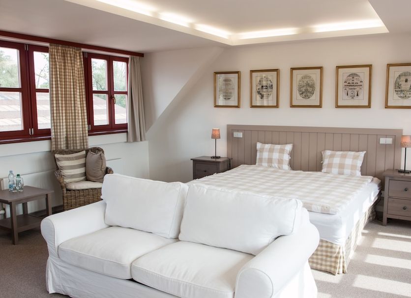 Dvur Hoffmeister in Kněževes: bright hotel room with white sofa, double bed, and framed wall art