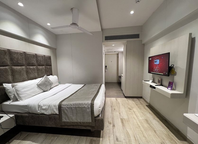 VITS Shalimar Ankleshawar room with king bed, wall-mounted TV, ceiling fan, and wood-look flooring in Ankleshwar