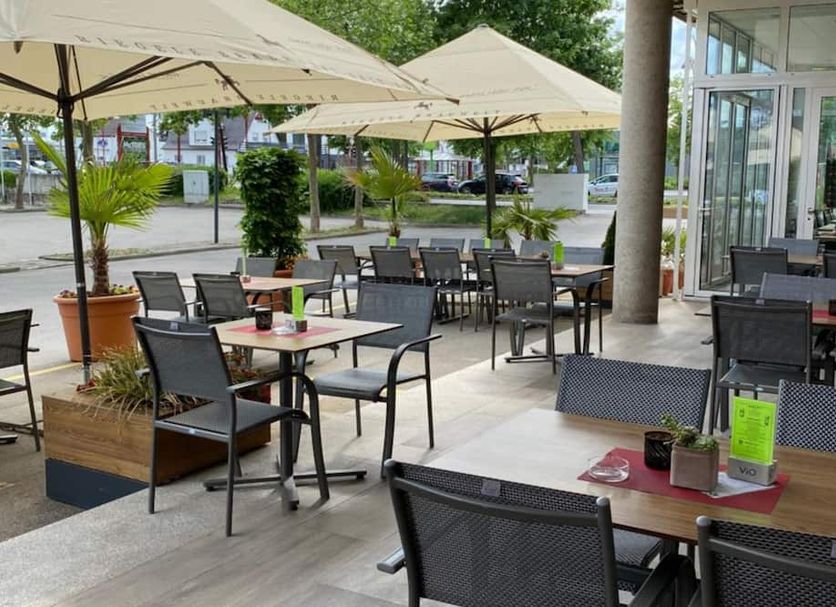 Outdoor terrace seating at Hotel Asgard in Gersthofen with umbrellas and tables by the entrance.