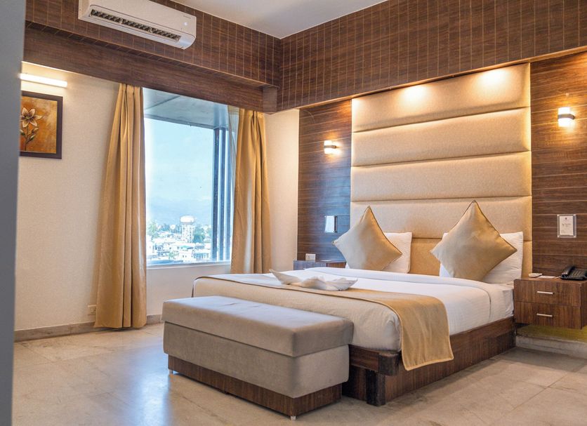 The Solitaire Hotel Dehradun room with king bed, bench, window city view and wood-paneled walls
