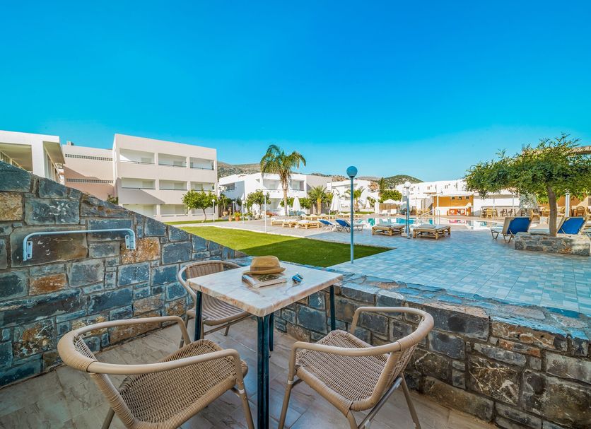 Maria Rousse in Mália: poolside seating, stone terrace, and resort buildings under a clear blue sky