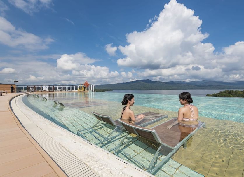 New Akan Hotel in Tsurui: infinity pool with lake view and two guests relaxing on lounge chairs