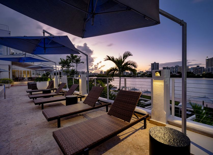 Hilton Garden Inn San Juan Condado rooftop terrace with lounge chairs, umbrellas and sunset city views