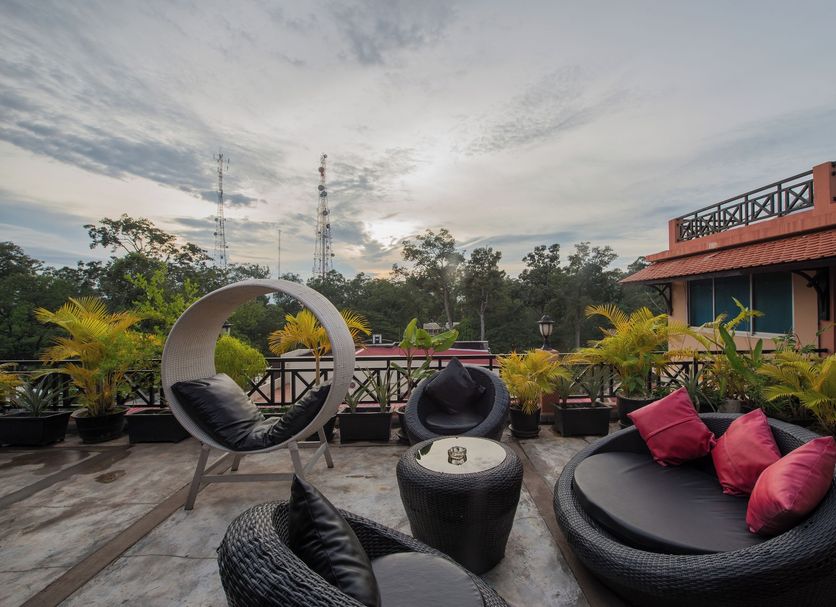 Jk Resident Siem Reap rooftop terrace with circular lounge chairs, potted plants, and sunset sky