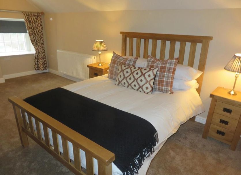 The Kings Head in Meifod: bedroom with wooden bed, bedside lamps, and a window with patterned curtains.