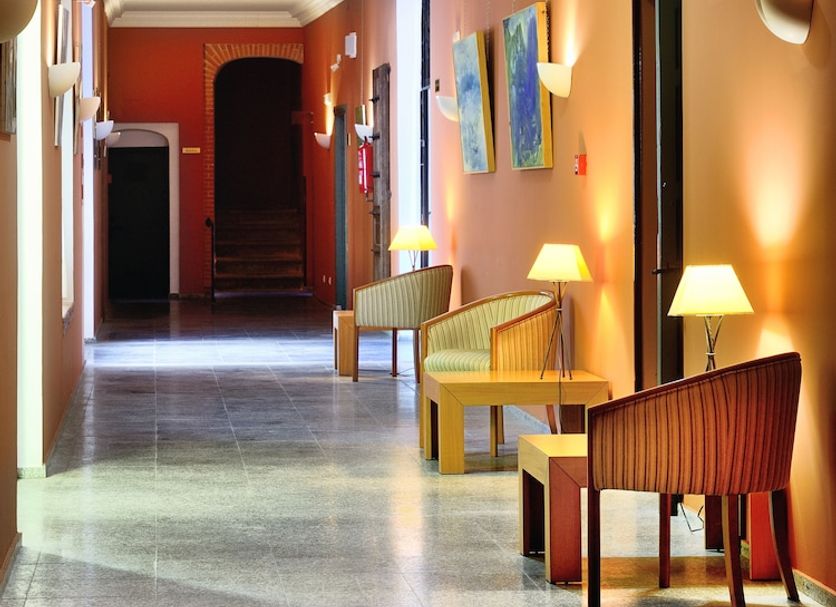 Hotel Ahc Palacio Coria hallway with orange walls, wall lights, chairs, and stone floor in Coria