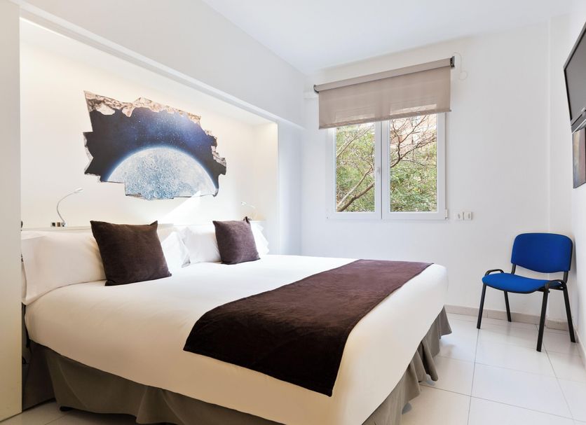 Hotel Travessera Barcelona guest room with double bed, wall art, window and blue chair