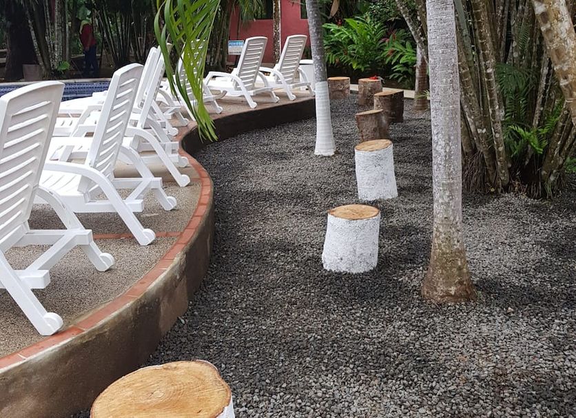 Hotel El Paraiso Escondido, Jacó: garden path with white lounge chairs and tree stump seats