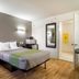 Studio 6-Plano, TX - Dallas - Plano Medical Center room with queen bed, wall lights, TV and bathroom door