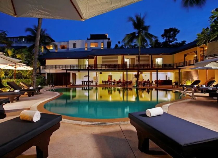 Bamboo Beach Hotel & Spa in Patong with a lit outdoor pool, palm trees and lounge chairs at dusk