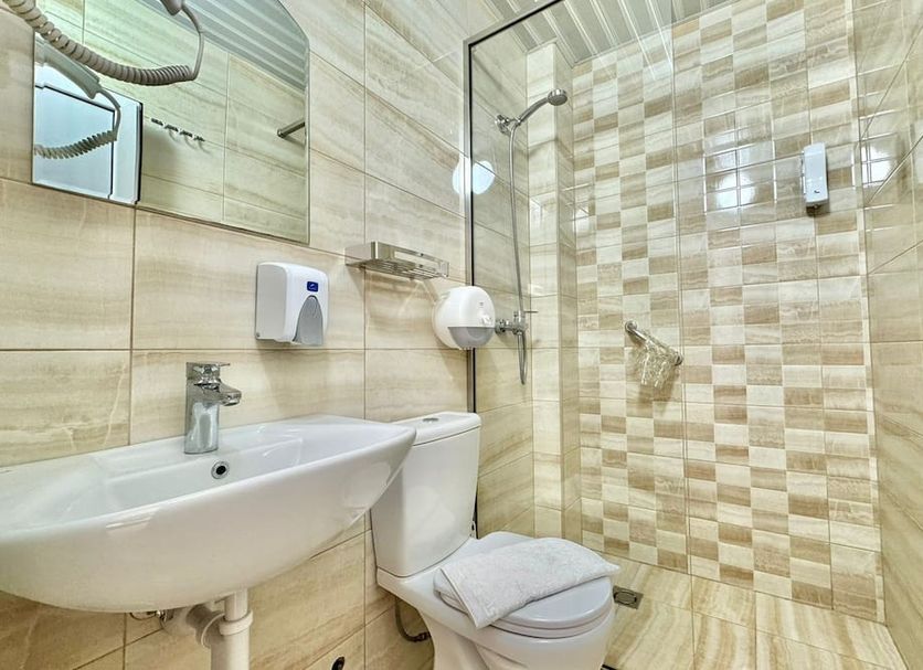 Hotel Grbalj in Budva bathroom with sink, toilet and glass shower with beige tile walls