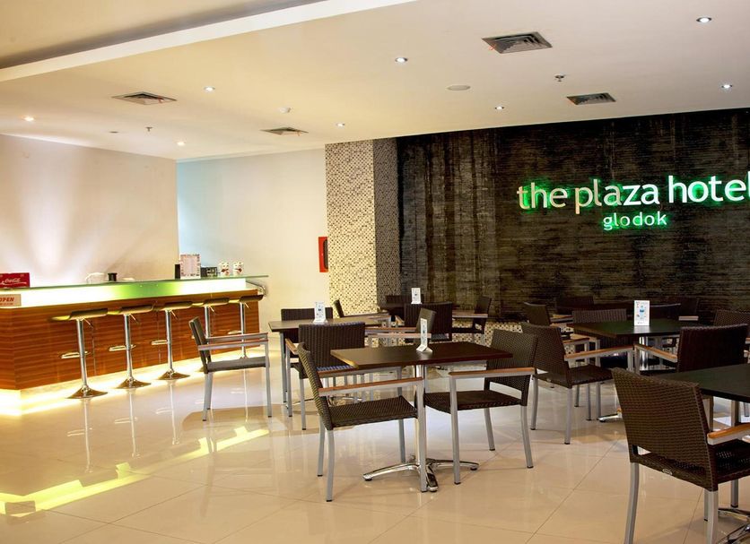 Lobby dining area at Hotel Glodok Plaza in Jakarta with tables, chairs and a lit bar