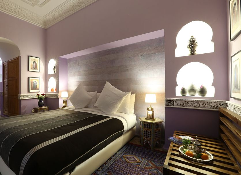 Riad Enchanté Marrakech bedroom with king bed, lavender walls, arched niches and serving tray