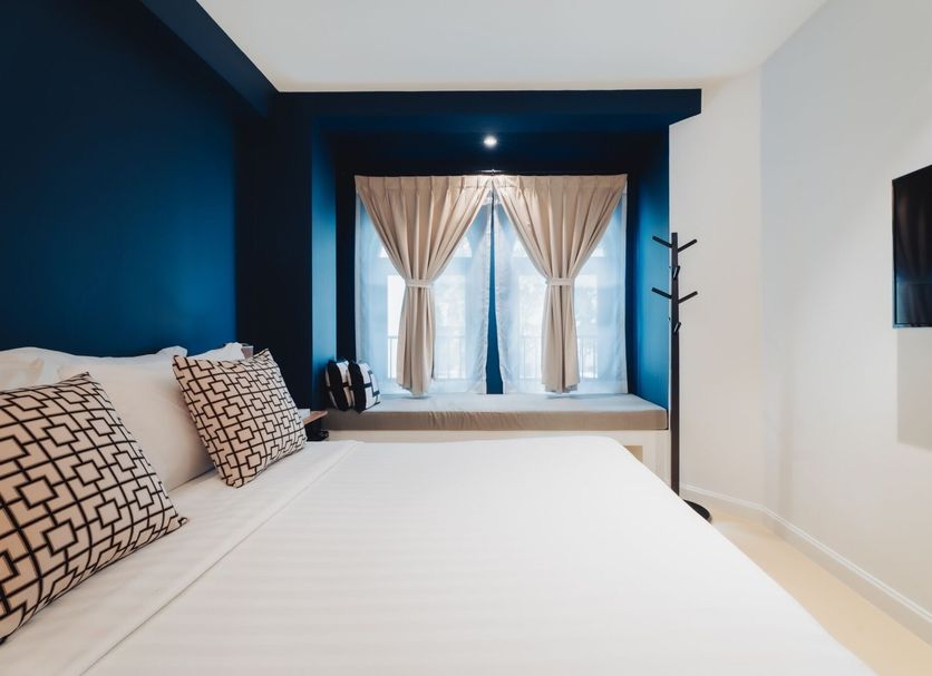 Xinlor House Phuket City guest room with blue accent wall, large window and patterned pillows