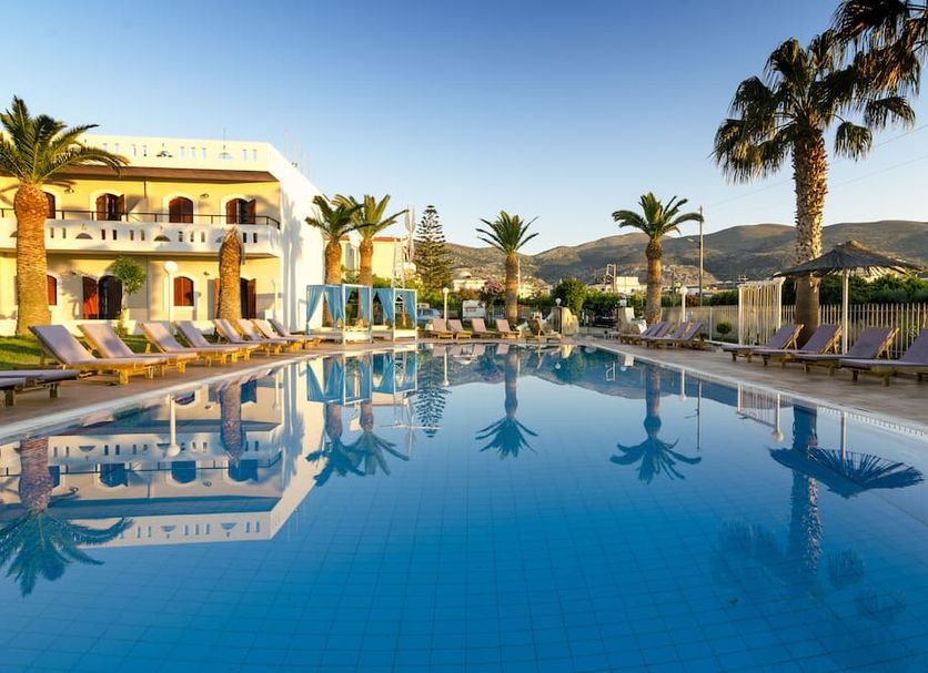 Stelios Gardens in Mália with a palm-lined outdoor pool and sun loungers beside a white hotel building