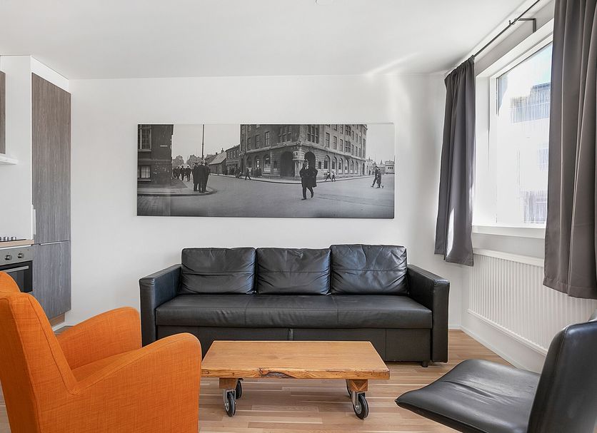 Stay Apartments Einholt Reykjavik apartment lounge with black sofa, orange chair, coffee table and window view