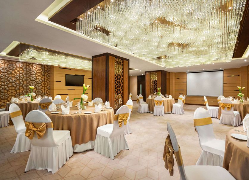 Wyndham Garden Manama banquet hall with round tables, white chairs, and a large projection screen