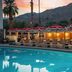 Royal Sun Palm Springs poolside lounge with palm trees, mountain backdrop, and lit cabanas at dusk